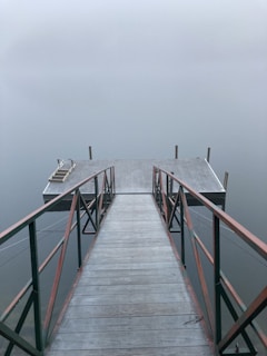 A serene morning view of a wooden jetty stretching into calm sea waters, with mist softly rolling over distant islands.
