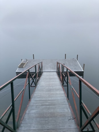 A serene morning view of a wooden jetty stretching into calm sea waters, with mist softly rolling over distant islands.