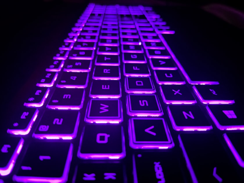 Purple and black mechanical gaming keyboard with RGB backlighting on a dark desk setup