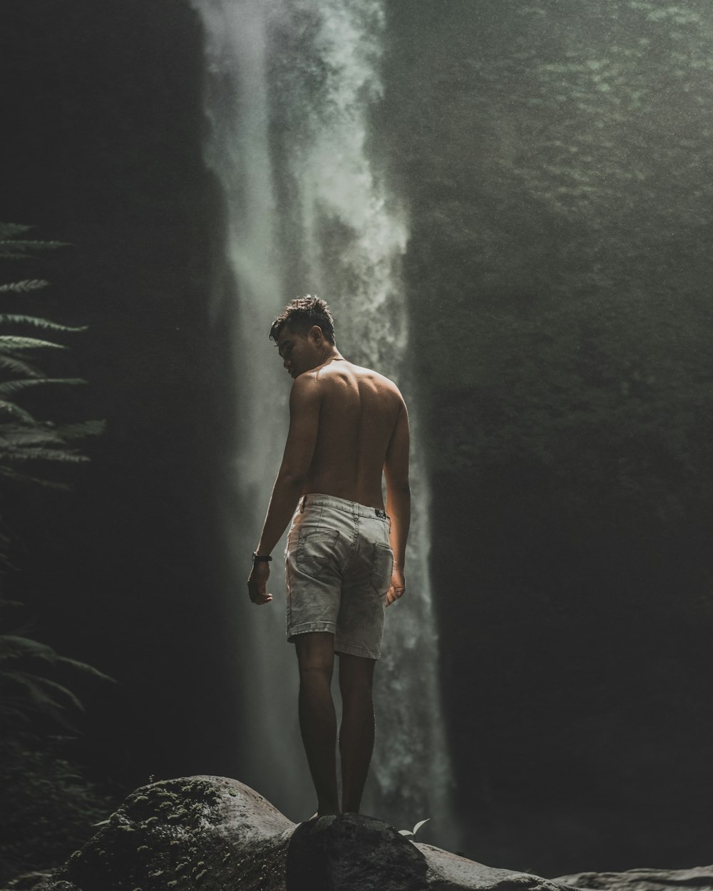 topless man in white shorts standing on rock in front of waterfalls