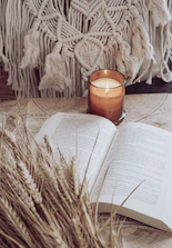 An open devotional book with a lit candle beside it on a wooden table.