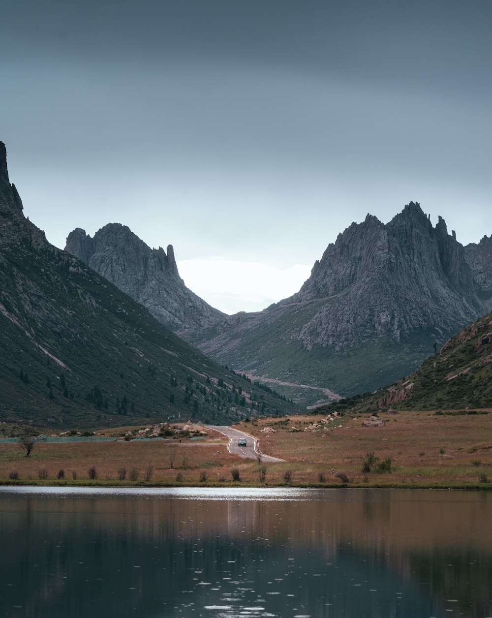 lake near mountain under white sky during daytime