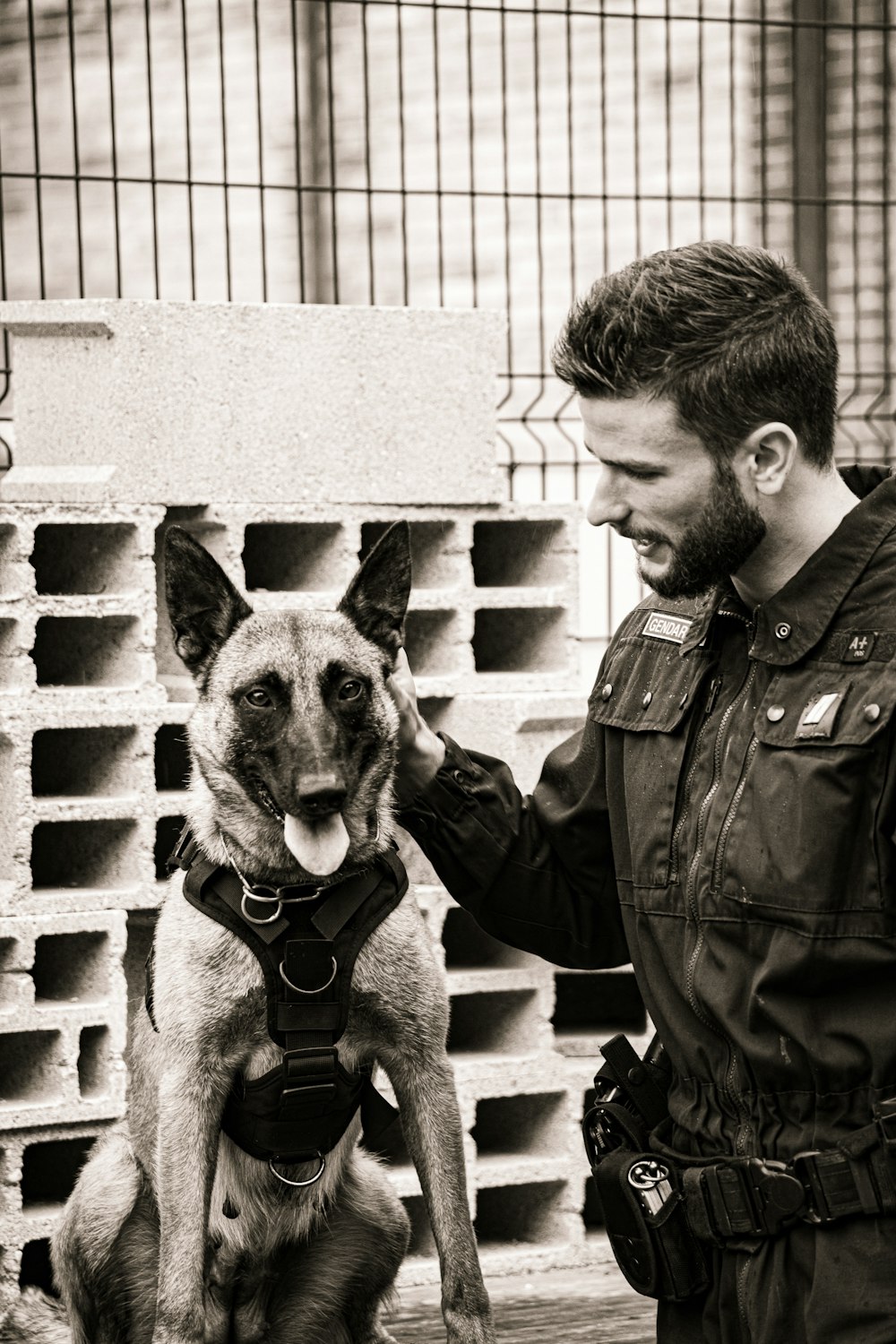 grayscale photo of man in police uniform carrying german shepherd