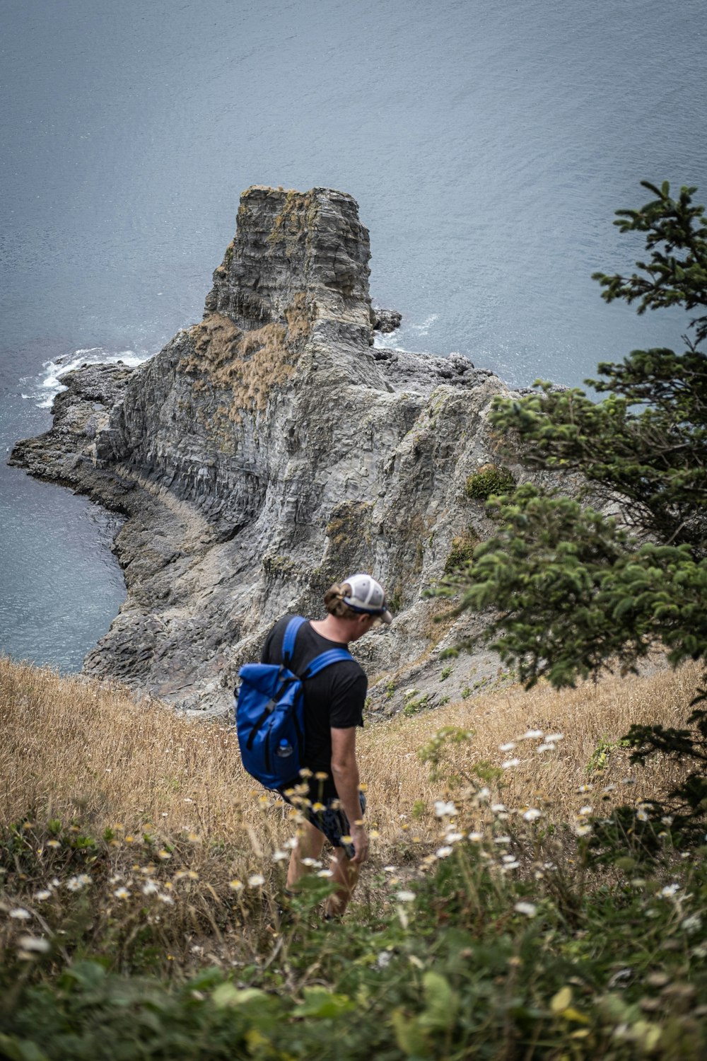 man in blue shirt and gray helmet standing on cliff near body of water during daytime