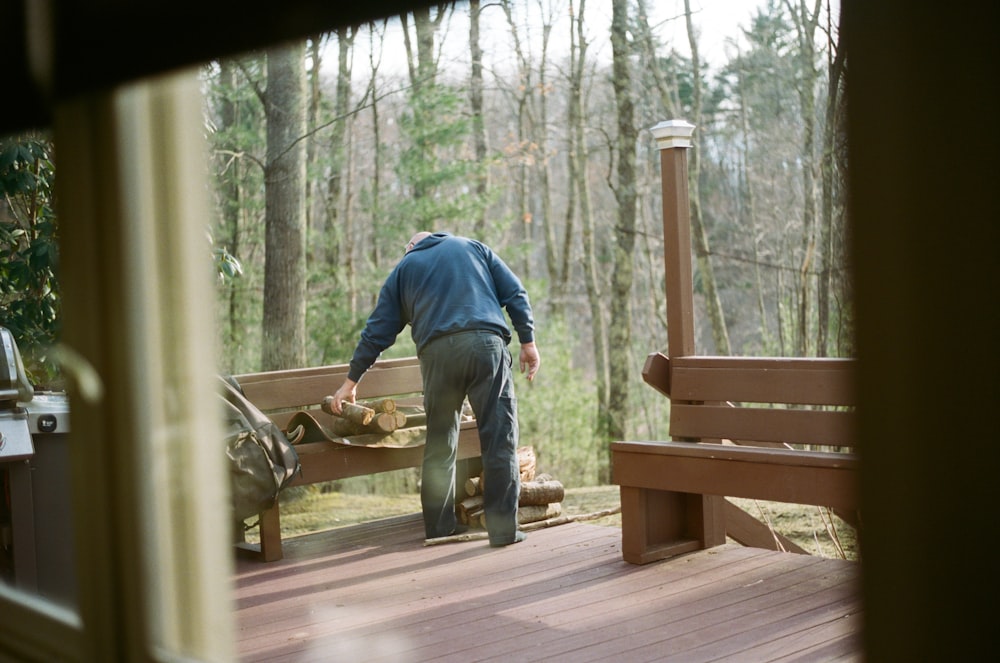 man in blue jacket and gray pants standing on brown wooden bridge