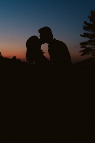 A romantic silhouette of the couple sharing a kiss on a cliffside with the sun dipping below the horizon.