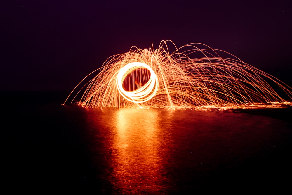 steel wool photography of person standing on body of water during night time