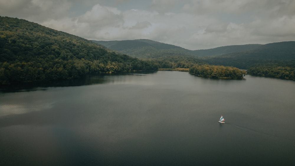 Bote blanco en el lago cerca de árboles verdes y montañas durante el día