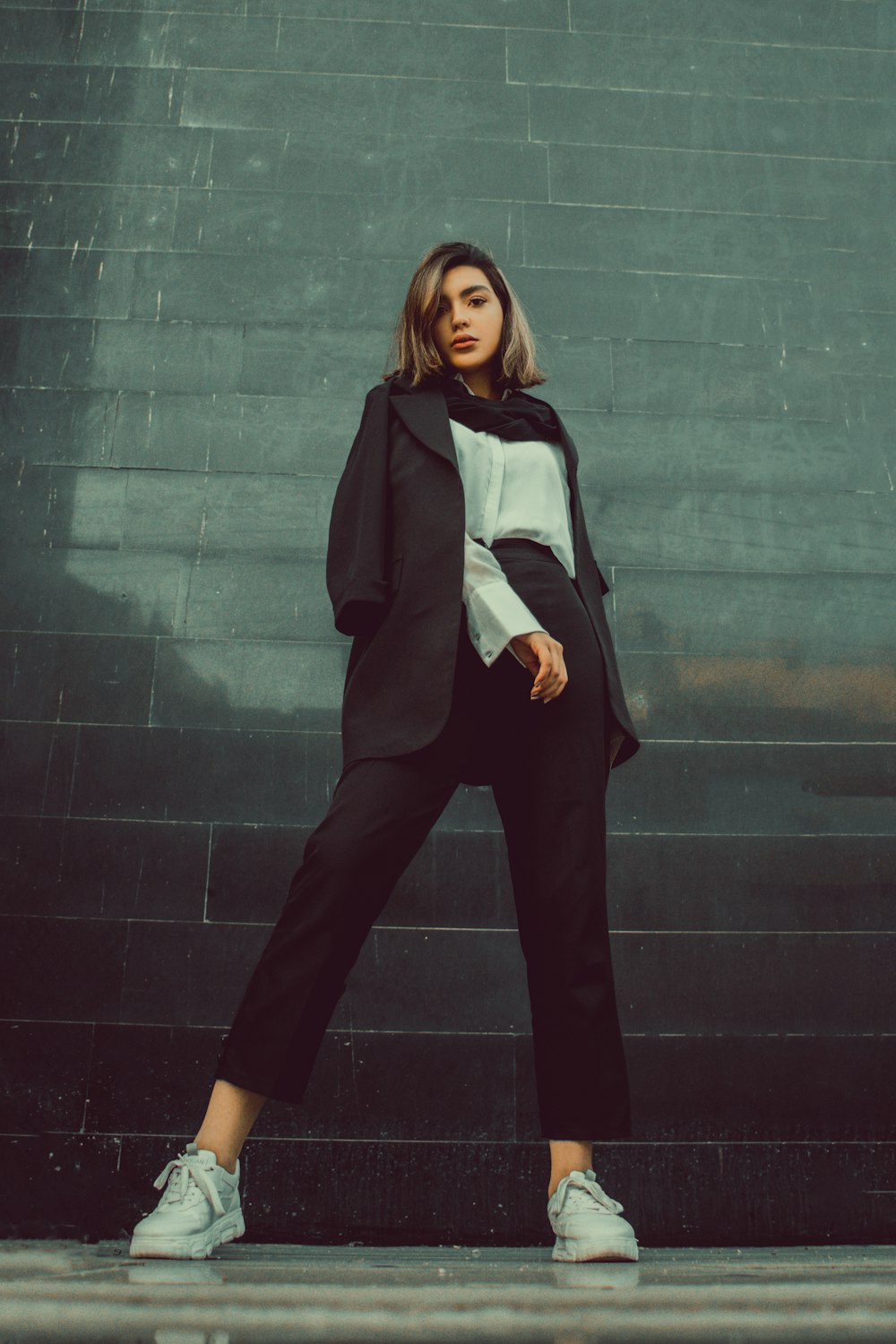 woman in black blazer and black pants standing beside green wall
