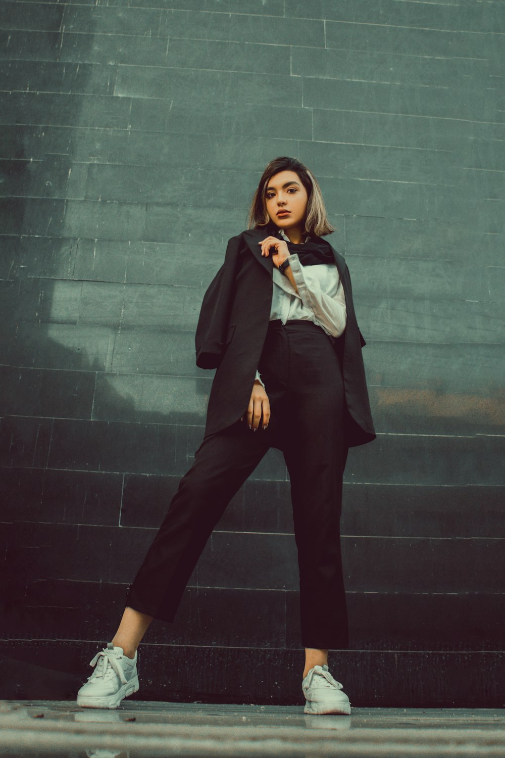 woman in black blazer and black pants standing beside gray wall