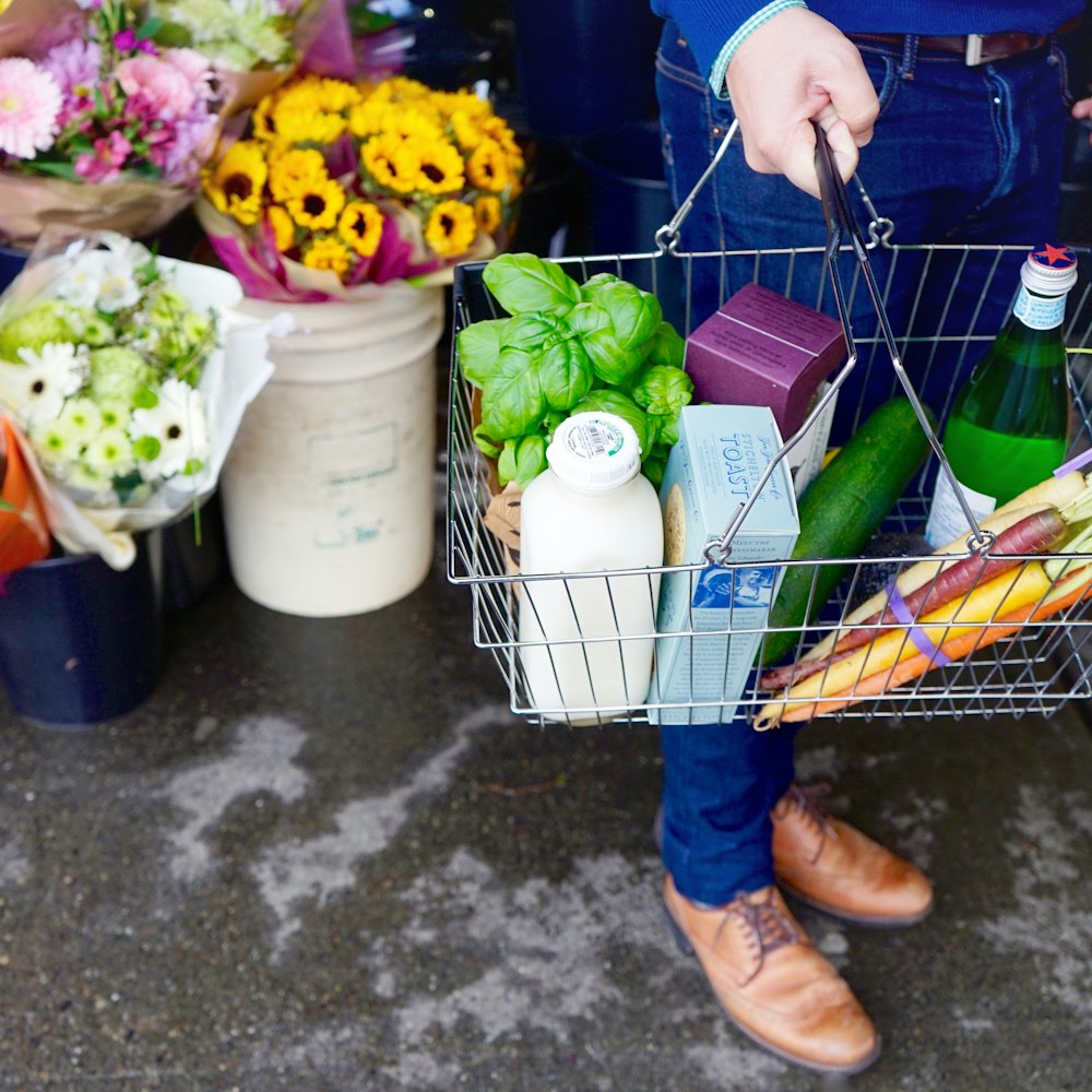 Person in blauen Jeans und braunen Lederstiefeln mit grüner Plastiktüte