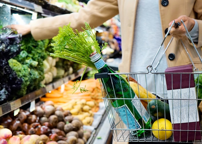 woman in white coat holding green shopping cart