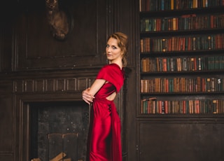 woman in red long sleeve dress standing beside brown wooden book shelf