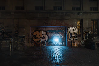 A nighttime shot of a city alley illuminated by a glowing Banksy piece.