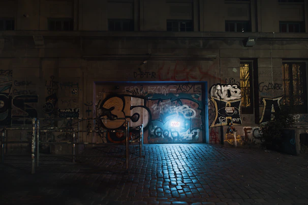 A nighttime shot of a city alley illuminated by a glowing Banksy piece.
