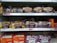 Several varieties of packaged bread are displayed on supermarket shelves. Brands such as Warburtons and Hovis are prominently visible, with loaves of wholemeal, seed sensations, and soft white varieties lined up in neat rows.