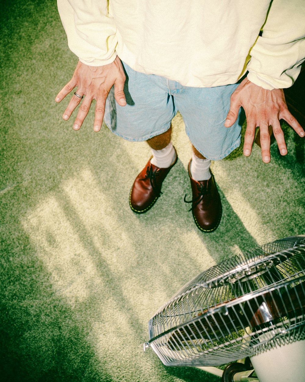 Person in weißem Hemd und blauen Jeansshorts auf grauem Teppich stehend