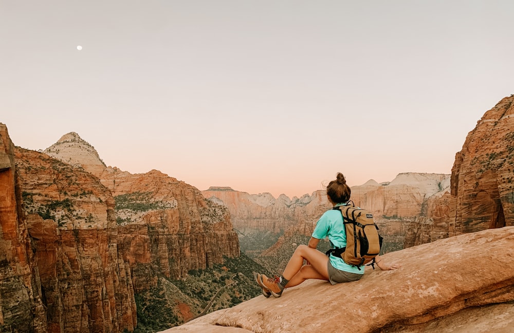 昼間、茶色の岩の上に座るティール色のタンクトップを着た女性
