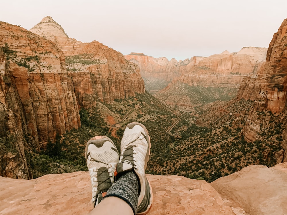 person in black shorts and white sneakers sitting on rock formation during daytime