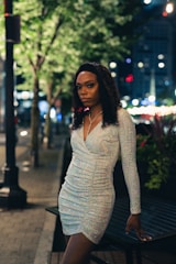 A glamorous model dressed in evening wear, standing against a city skyline at night.
