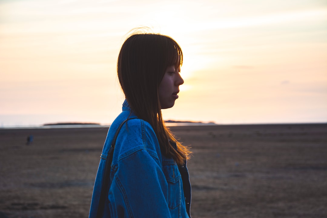 woman in blue jacket standing on field during sunset