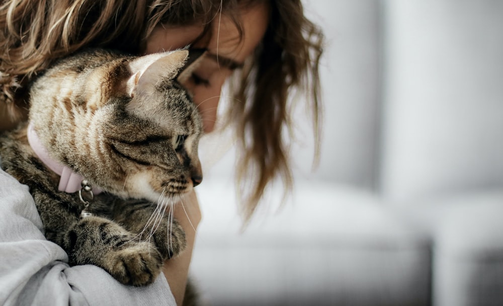 woman in white tank top carrying brown tabby cat