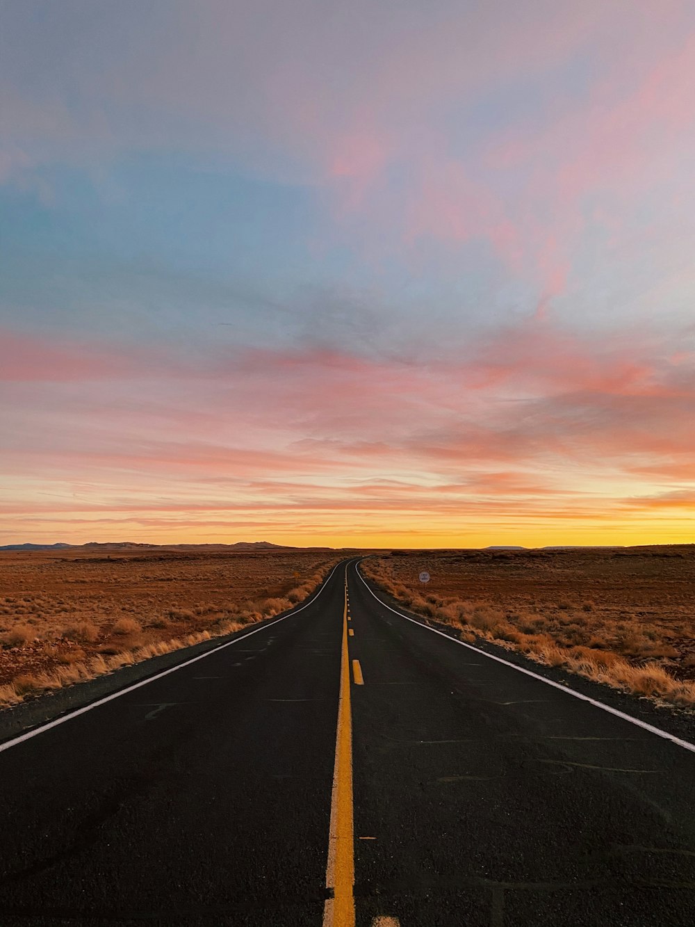 black asphalt road between brown field during sunset