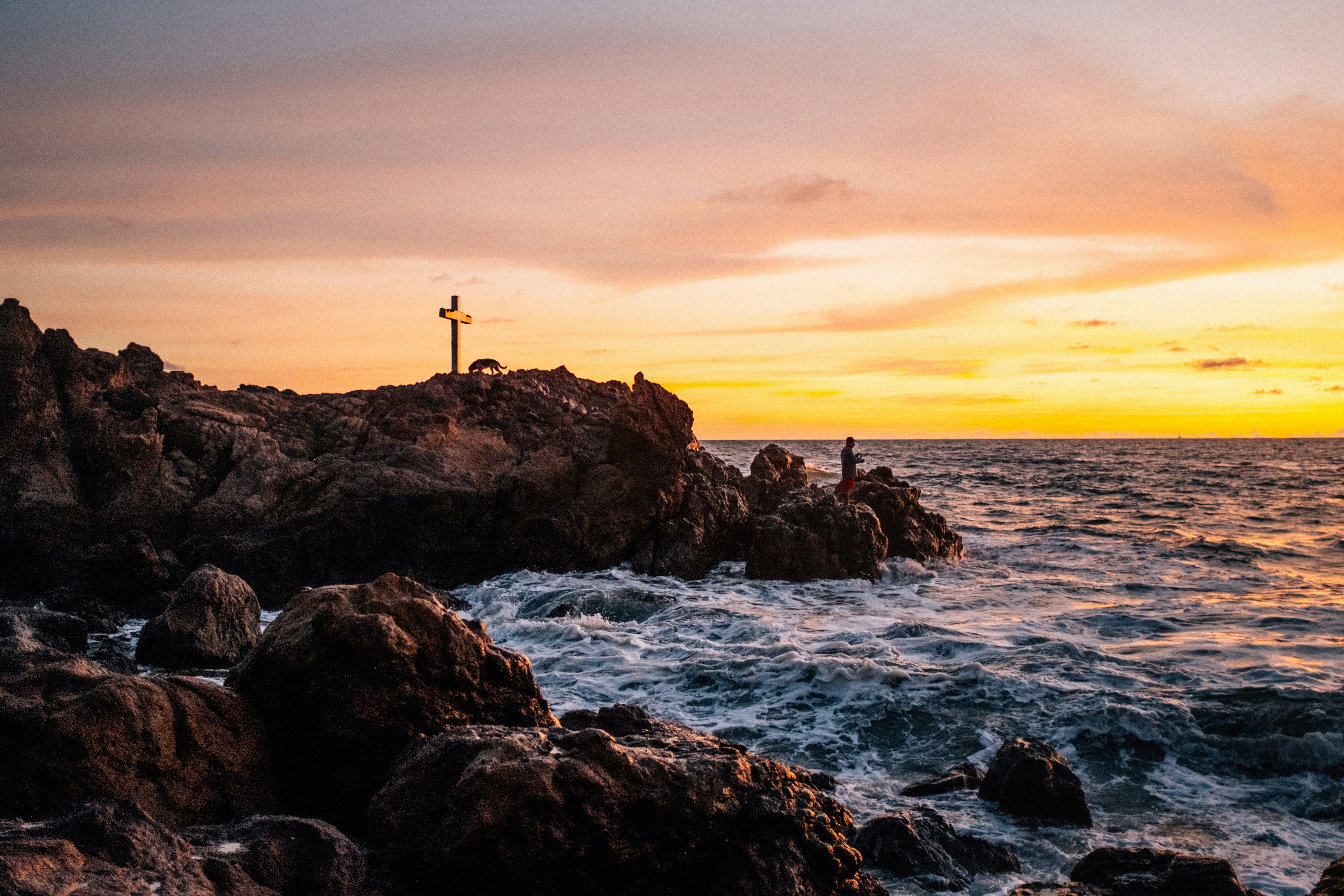 silhouette of person standing on rock formation near body of water during sunset, 