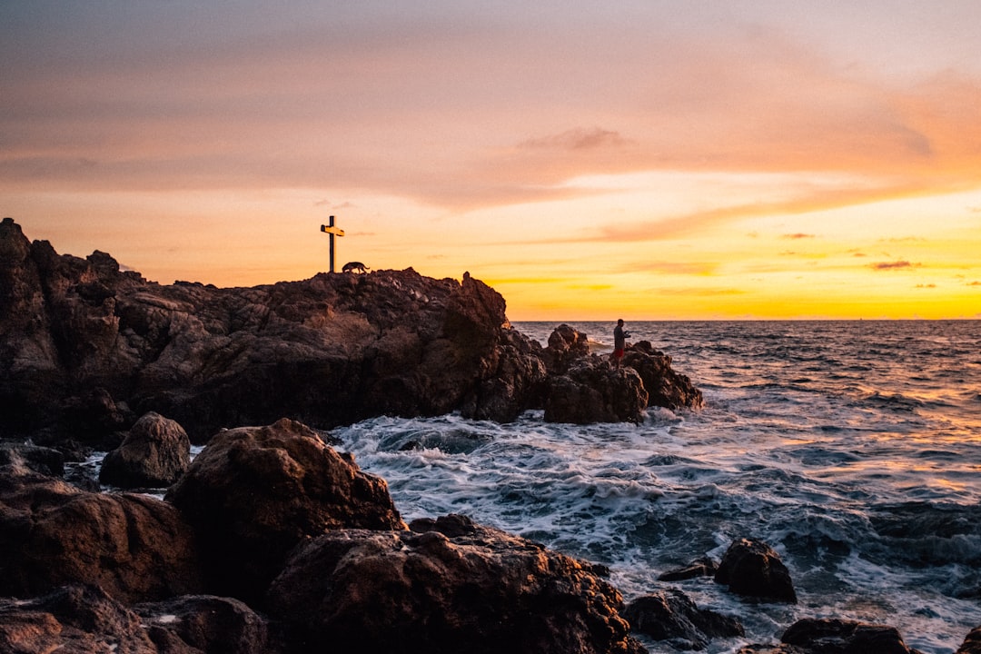 silhouette of person standing on rock formation near body of water during sunset