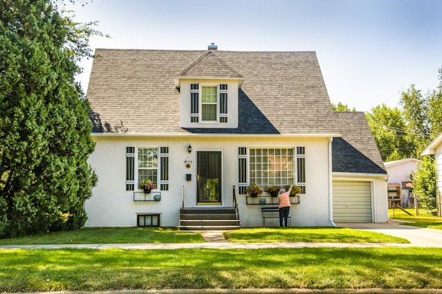 A friendly real estate agent smiling warmly in front of a charming suburban home.