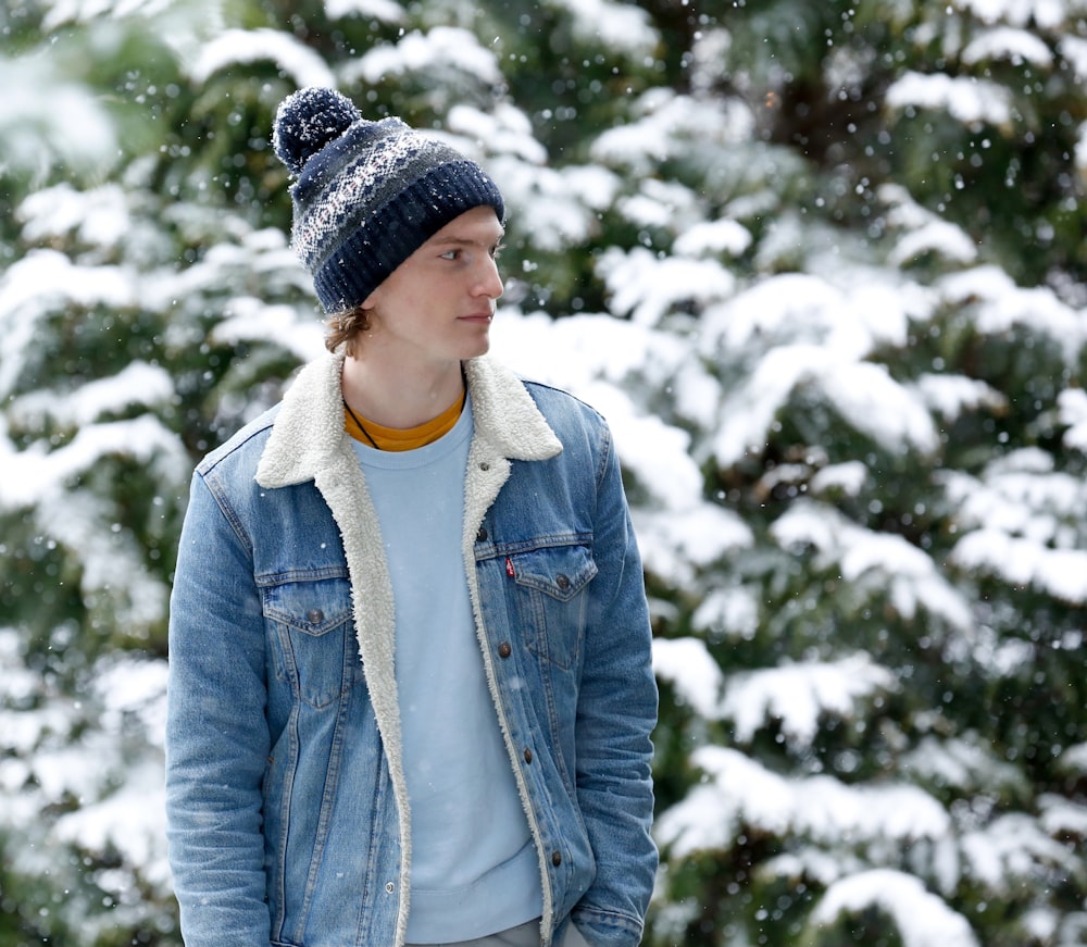 woman in blue denim jacket and black knit cap standing near snow covered trees during daytime