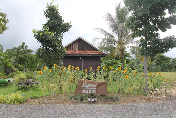 A warm, inviting Cambodian home surrounded by lush greenery and solar panels on the roof.