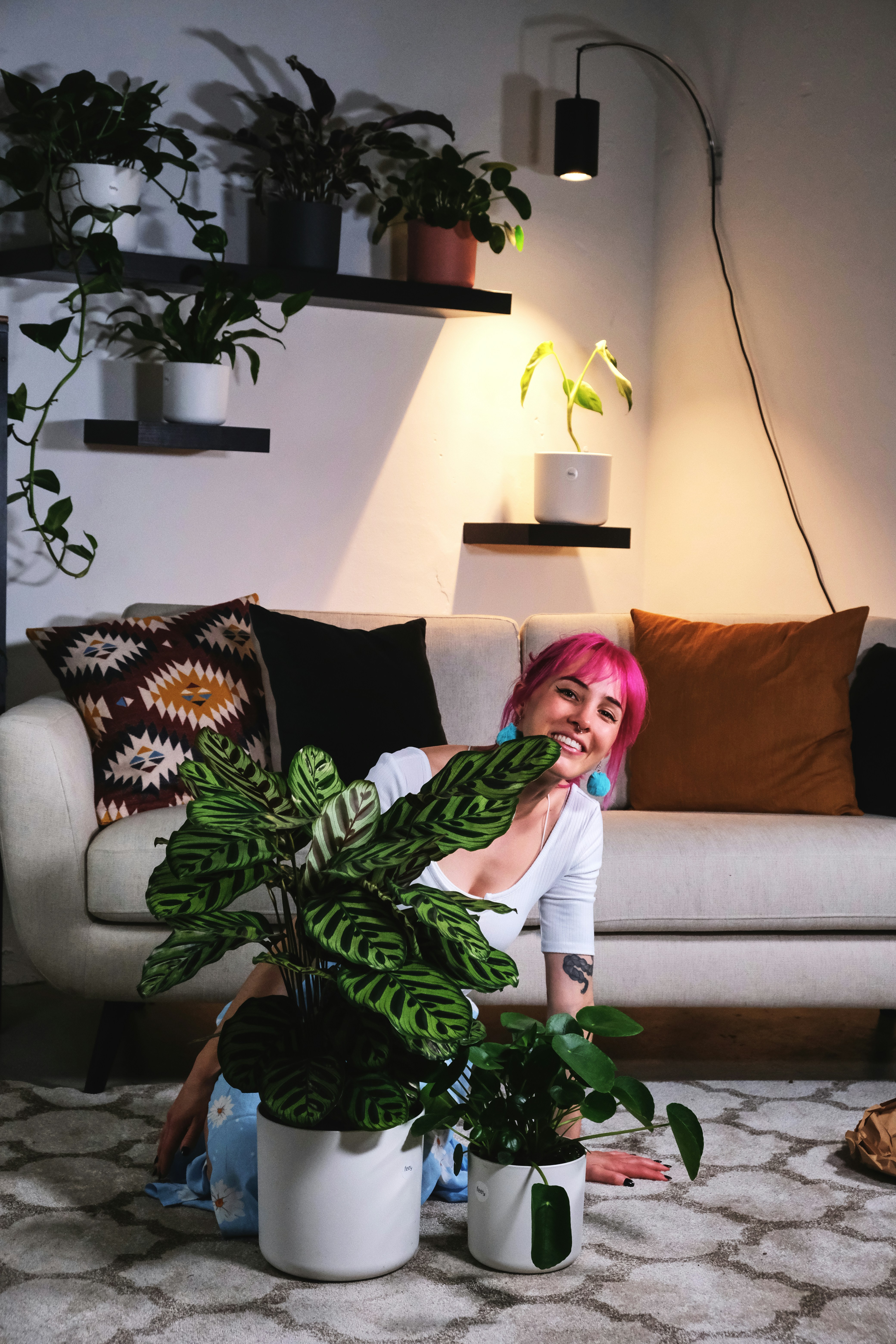 Woman with pink hair sitting on the floor behind two feey plants