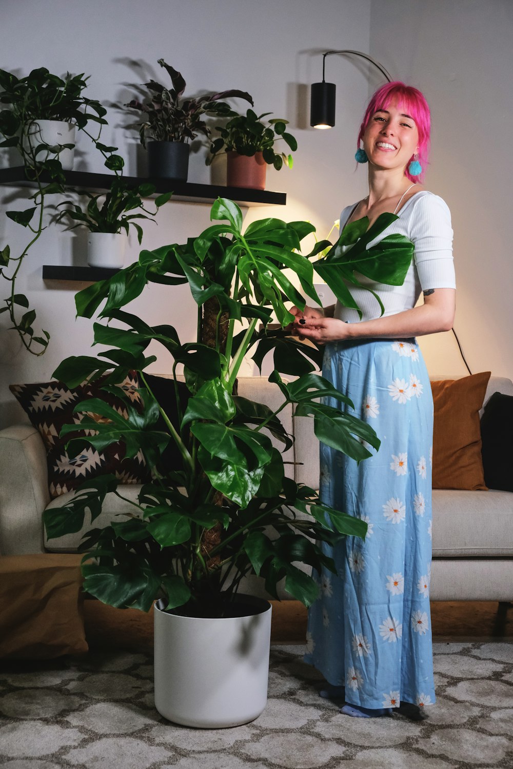 woman in white t-shirt and blue and white floral skirt standing beside green plant