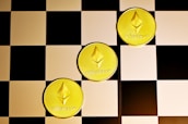 Three gold coins with the Ethereum logo and text are placed diagonally on a black and white checkerboard surface.