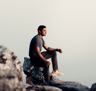 man in black t-shirt and brown pants sitting on rock during daytime