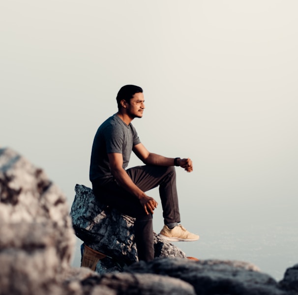 man in black t-shirt and brown pants sitting on rock during daytime