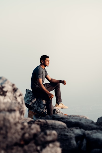 man in black t-shirt and brown pants sitting on rock during daytime