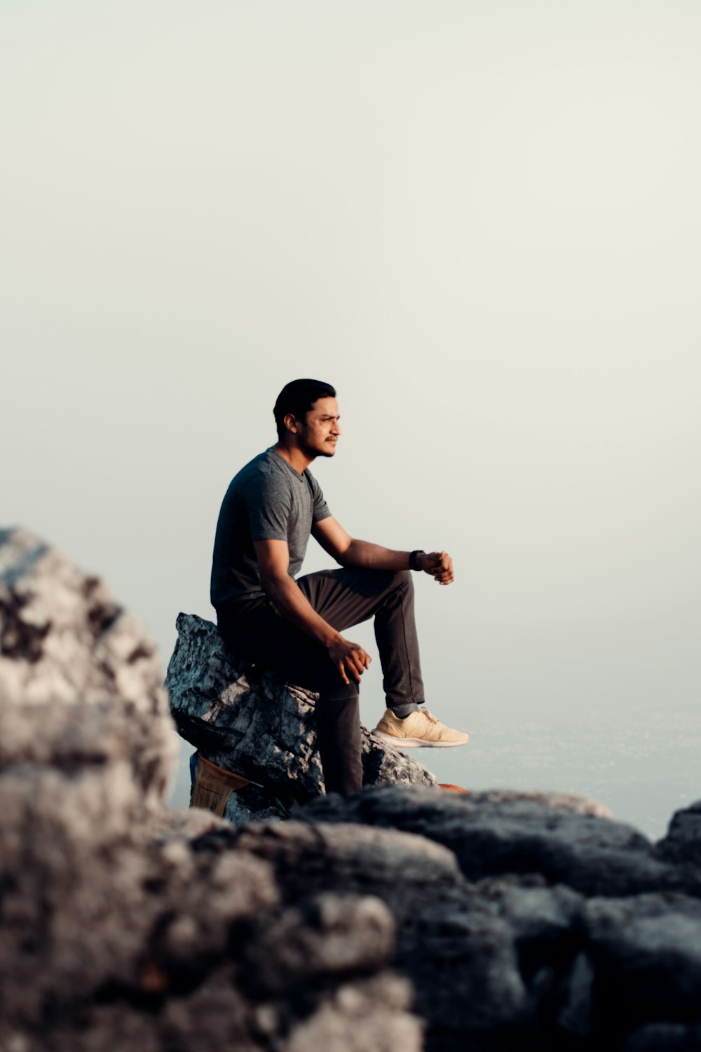 man in black t-shirt and brown pants sitting on rock during daytime