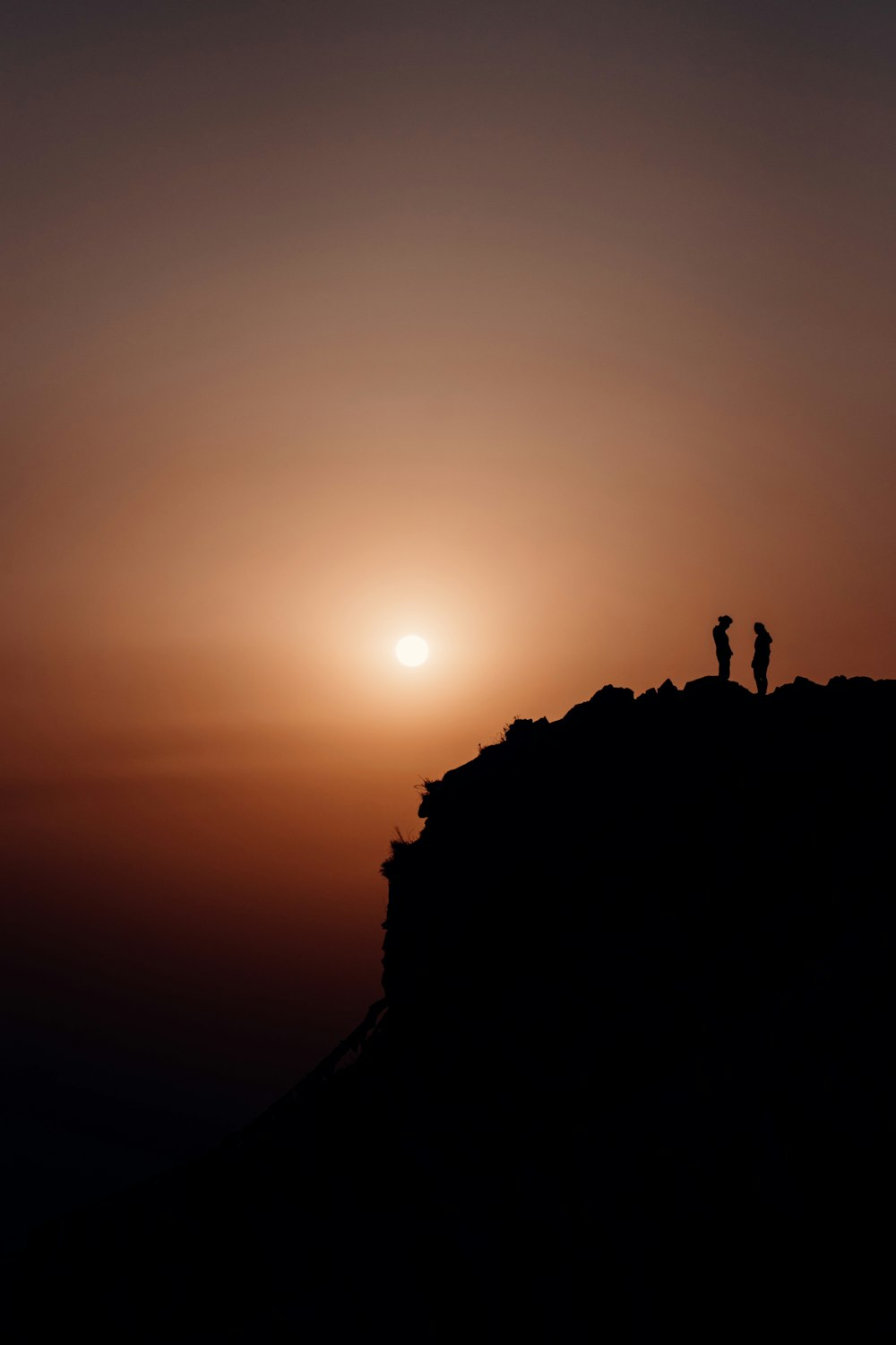 silhouette of 2 people standing on rock formation during sunset