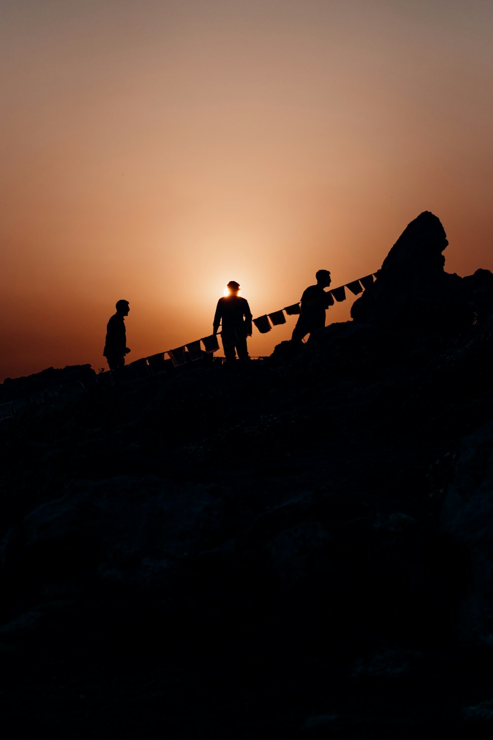 silhouette de personnes debout sur la formation rocheuse au coucher du soleil