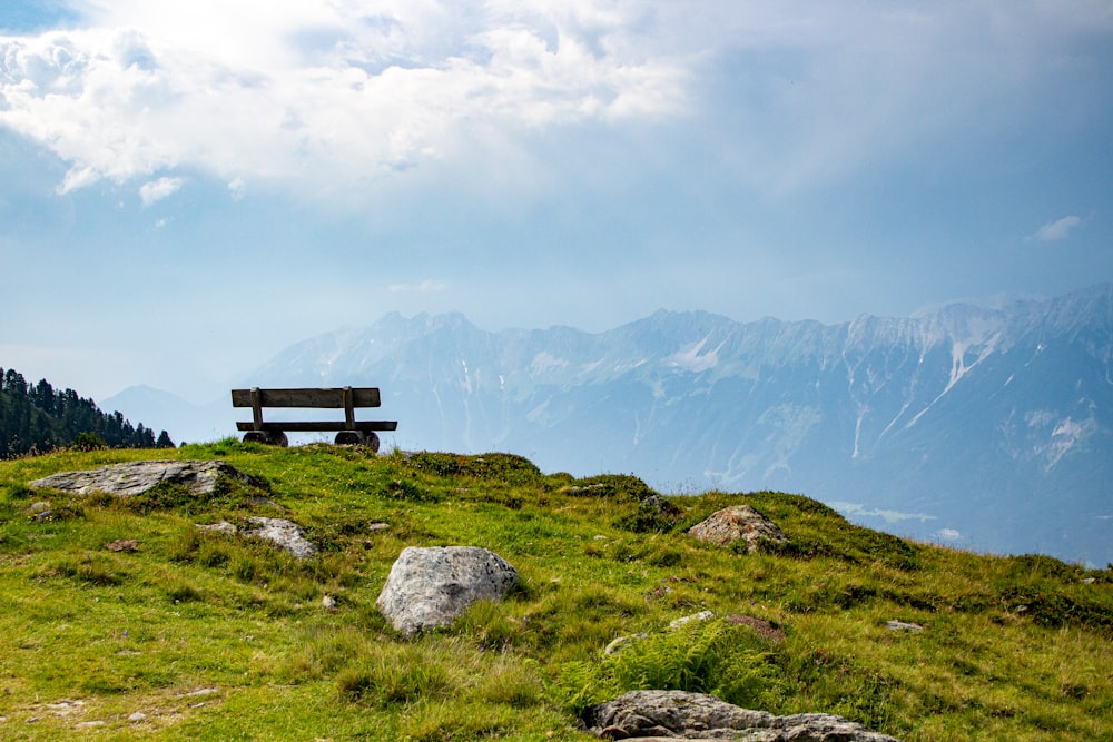 black wooden bench on green grass field near mountains during daytime