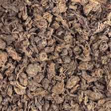 Dry, crumpled tea leaves form a densely packed texture. The leaves are dark and appear aged, with a mix of curled and twisted shapes.