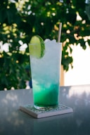 clear drinking glass with blue liquid and sliced of lime