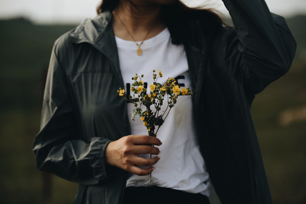 woman in black jacket holding yellow flowers