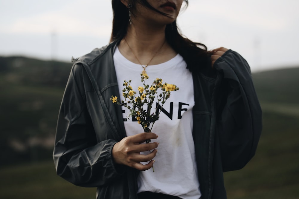 woman in white crew neck shirt and black jacket holding yellow flowers