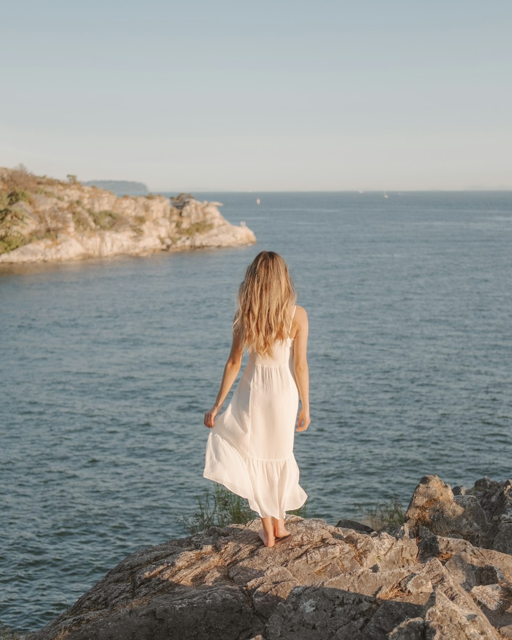낮 동안 수역 근처의 바위에 서 있는 하얀 드레스를 입은 여자