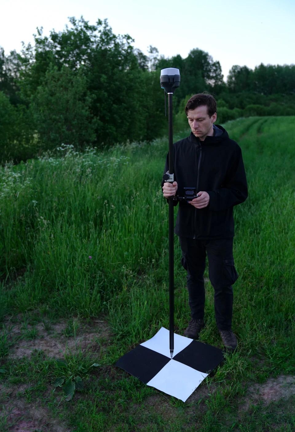 A surveyor working with a measuring pole on open grassland