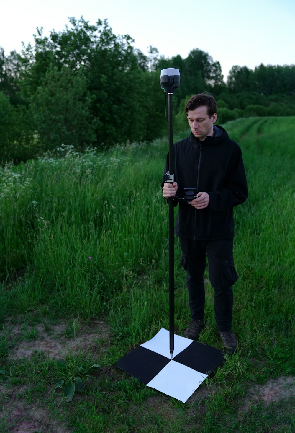 homme en veste noire tenant un bâton noir debout sur un champ d’herbe verte pendant la journée