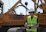 man in green and yellow vest standing beside orange and black heavy equipment